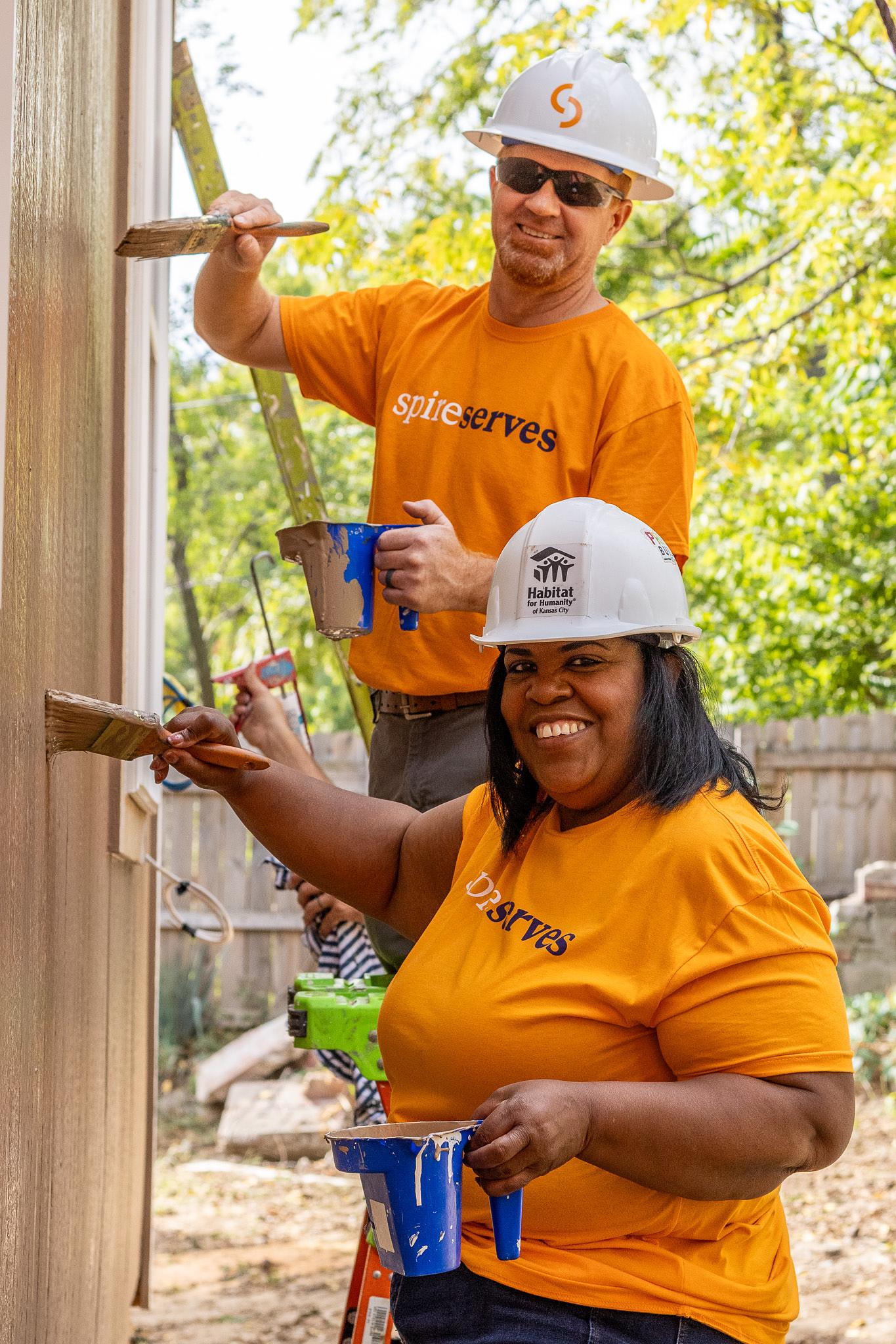 two Spire employees smiling while painting a house