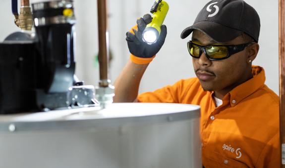 Image of Spire service technician working on a furnace. He is holding a flashlight and wearing a Spire uniform.