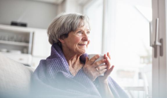 Image of elderly woman drinking coffee wrapped in a purple blanket