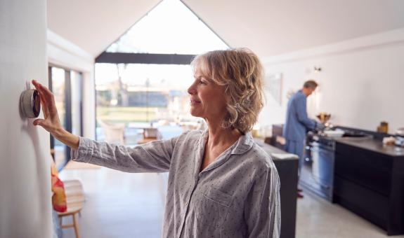 Image of woman adjusting smart thermostat inside her home