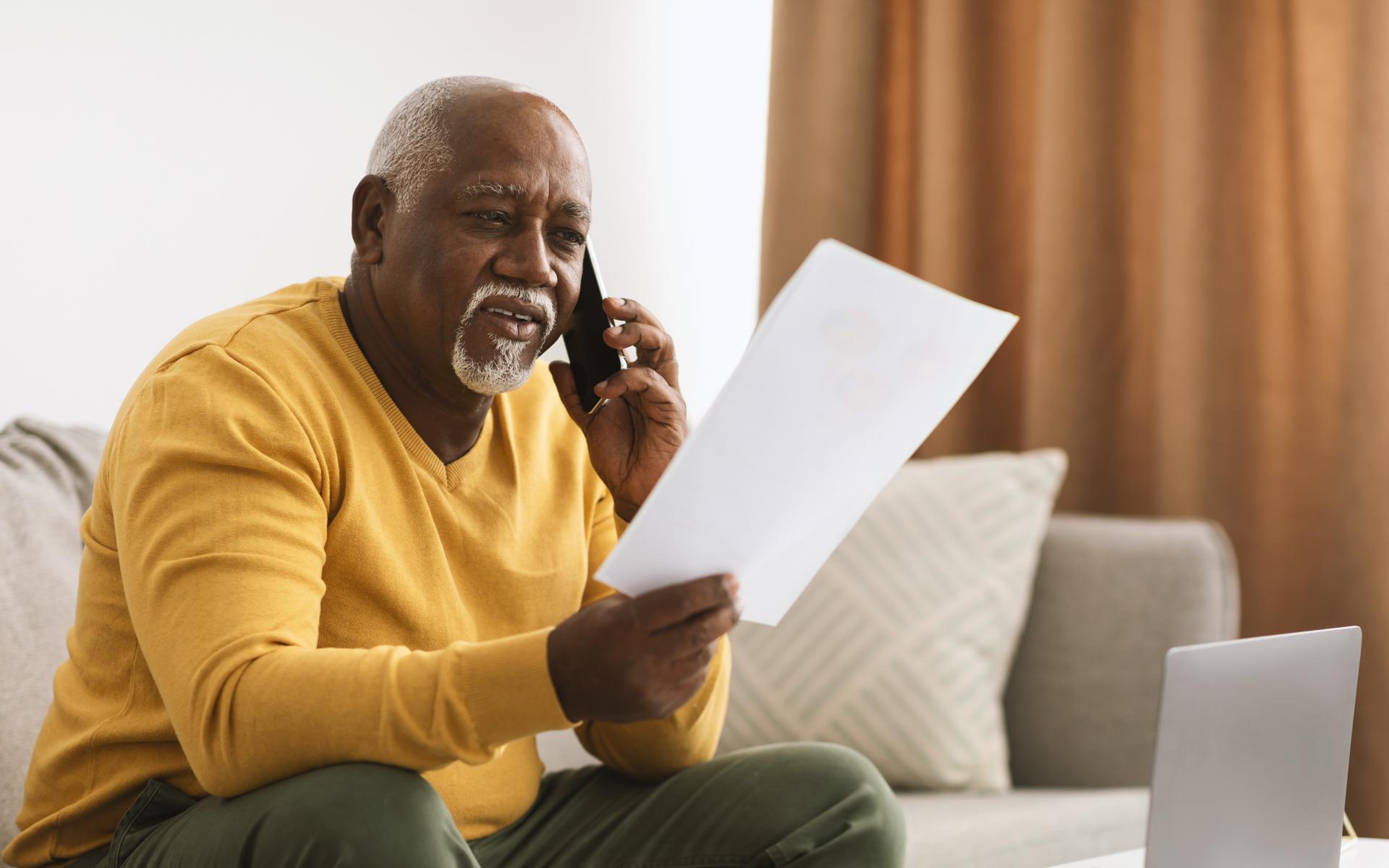Image of gentleman wearing a yellow sweatshirt reading a paper and talking on the phone
