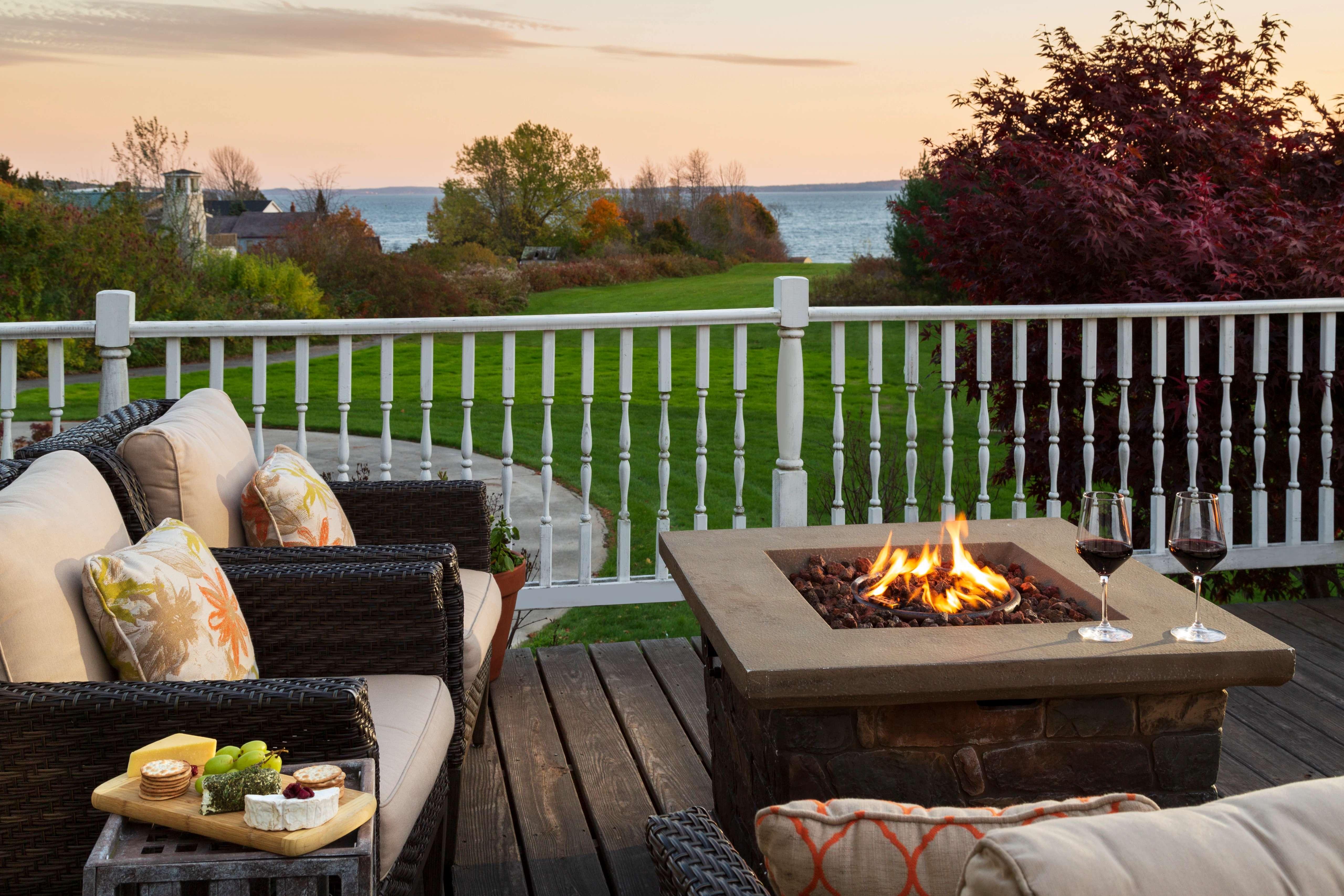 Image of a back deck overlooking a lake. There's a fireplace and cozy outdoor appliances.
