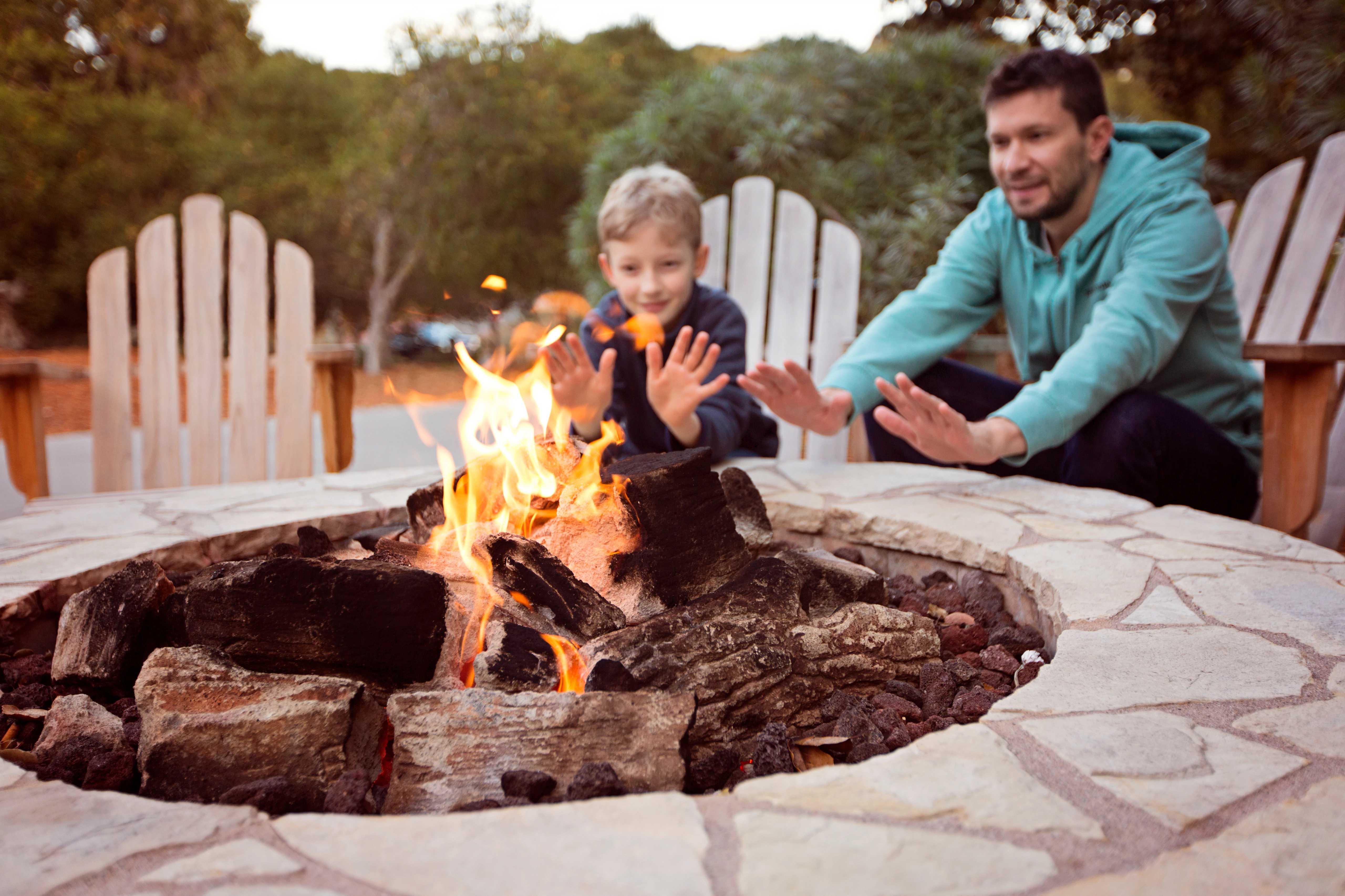 Image of father and son warming their hands around a fireplace outside
