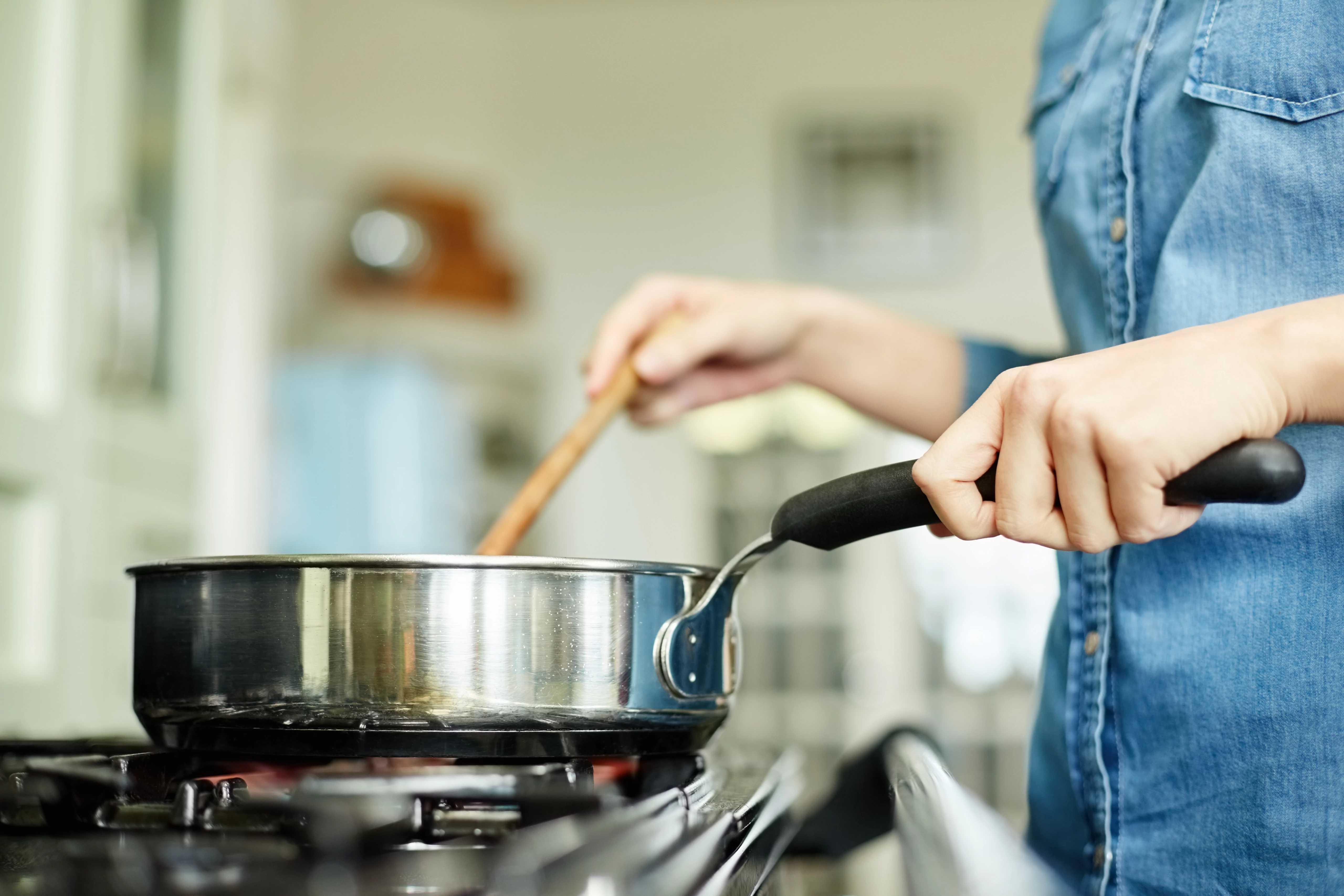 Image of a hand stirring a pot on a natural gas stove